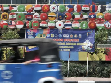 Bajaj melintas di depan instalasi berupa bendera negara-negara peserta Asian Games 2018 di Jalan Tanah Tinggi Barat, Kelurahan Bungur, Kecamatan Senen, Jakarta, Minggu (15/7). (Merdeka.com/Iqbal S. Nugroho)