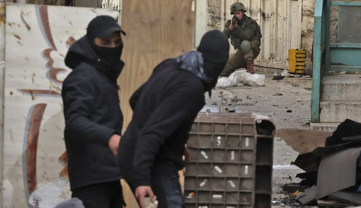 Seorang tentara Israel membidik sementara seorang pengunjuk rasa Palestina bersiap untuk melempar batu saat bentrokan di pusat Kota Hebron, Tepi Barat, 4 Maret 2022. (HAZEM BADER/AFP)