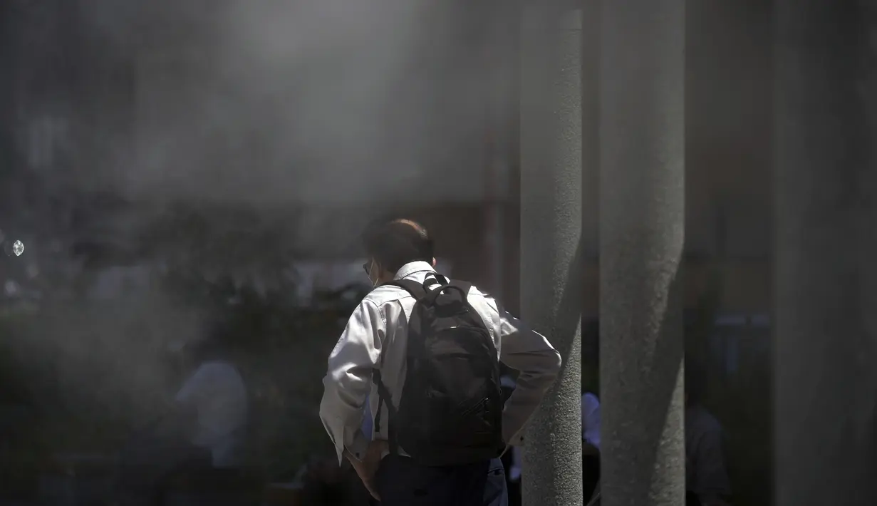 Seorang pria memakai masker untuk membantu melindungi dari penyebaran virus corona mendingin di titik kabut dingin di Tokyo, Selasa (28/6/2022). Pejabat cuaca juga mengumumkan akhir paling awal musim hujan dalam beberapa dekade. (AP Photo/Eugene Hoshiko)