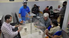 Pramusaji mengenakan pelindung wajah dan masker saat menyajikan makanan kepada pelanggan di restoran yang dibuka kembali usai pelonggaran lockdown di Bangalore, India, Senin (8/6/2020). Untuk keamanan pelanggan, restoran-restoran menyiapkan panel transparan di meja makan. (Manjunath Kiran/AFP)