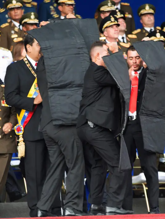Pengawal melindungi Presiden Venezuela Nicolas Maduro dengan perisai antipeluru saat serangan drone di Caracas, Venezuela, Sabtu (4/8). Tujuh tentara dilaporkan terluka dalam serangan tersebut. (Xinhua via AP)