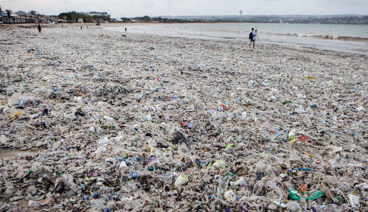 Volume sampah kiriman mencapai puluhan ton per hari, yang didominasi oleh limbah plastik dan potongan kayu. Tampak dalam foto, para pekerja dan warga membersihkan ceceran dan tumpukan sampah plastik yang terdampar di Pantai Jimbaran, Bali, pada Selasa 10 Maret 2026. (Lana Priatna/AFP)