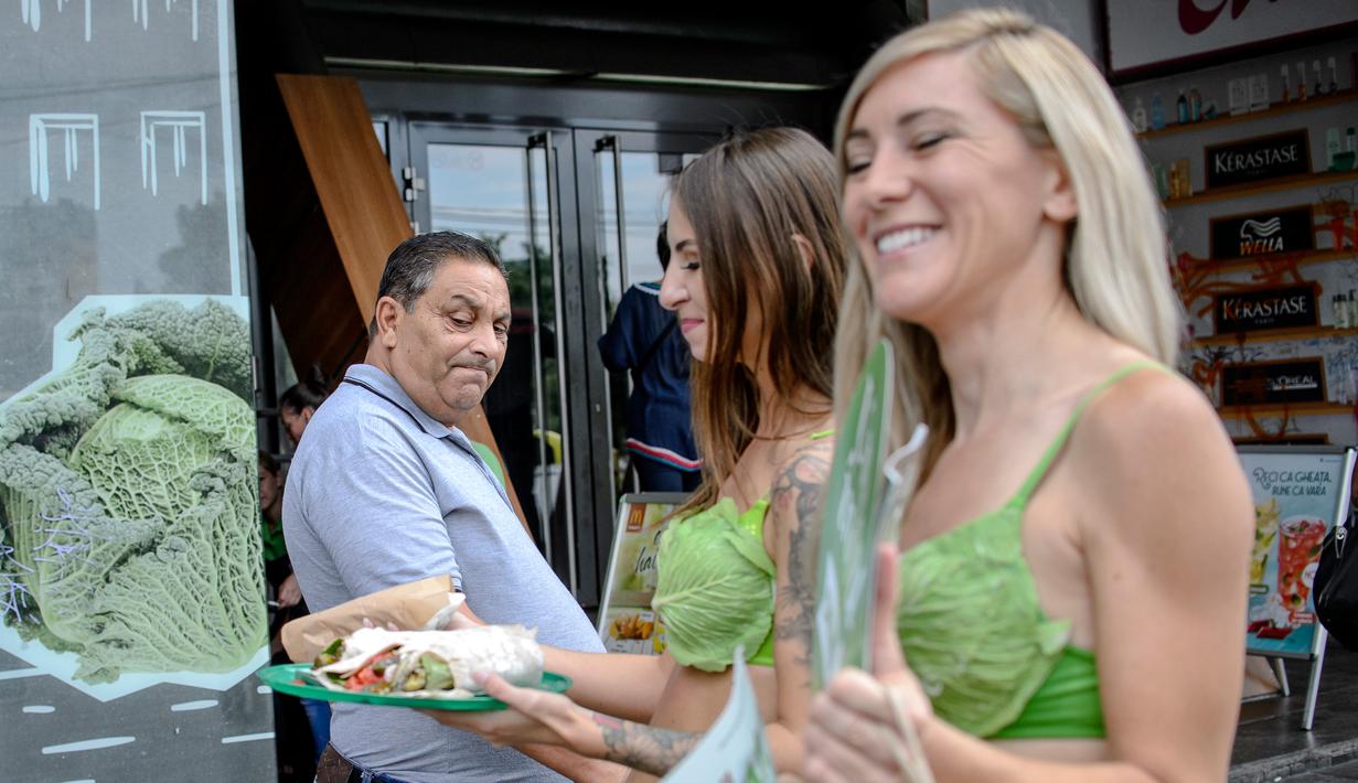 Seorang pria melihat makanan yang dibawa dua aktivis wanita dari PETA saat berkampanye gaya hidup vegan di pusat kota Bucharest, Rumania, (14/8). Kampanye hidup vegan ini akan berlanjut ke negara AS, Rusia da Turki. (AP Photo/Andreea Alexandru)