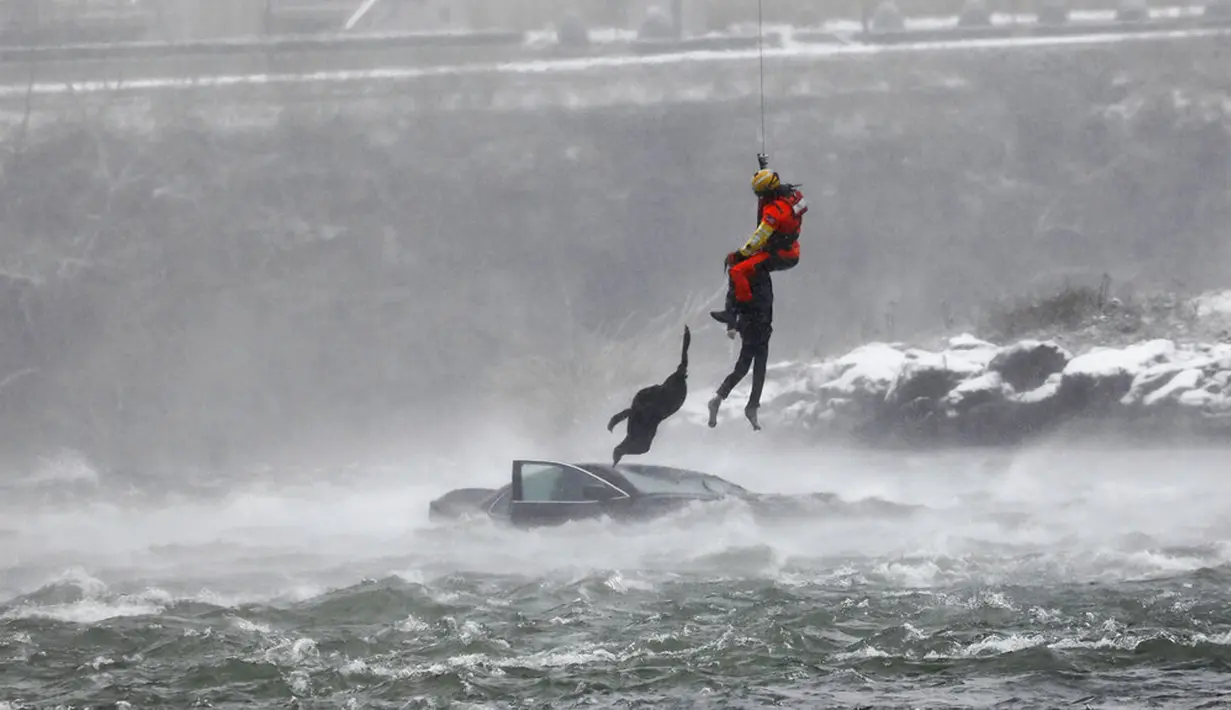 Penyelam Penjaga Pantai AS diturunkan dari helikopter untuk menarik tubuh pengendara mobil yang terjebak dalam arus deras di tepi Air Terjun Niagara, New York, AS, 8 Desember 2021. Penyelamat mendobrak pintu sisi penumpang untuk melakukan evakuasi. (Derek Gee/The Buffalo News via AP)
