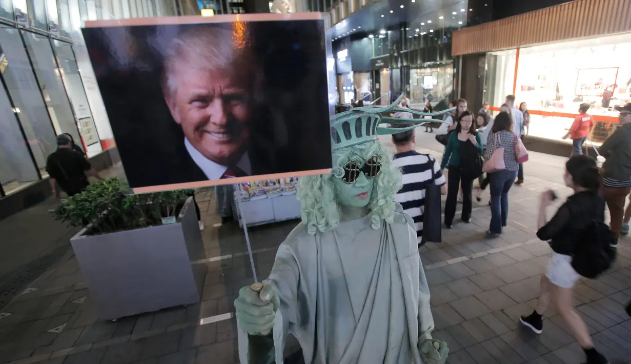Seorang seniman jalanan berpakaian seperti Patung Liberty, memegang gambar Presiden terpilih AS, Donald Trump di pusat kota Hong Kong, Rabu (9/11). (AP Photo / Kin Cheung)