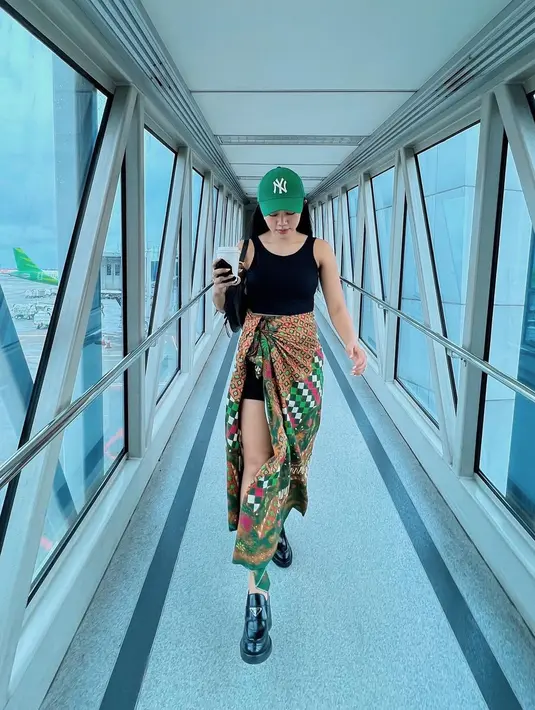 <p>Siapa bilang kain batik tak bisa digunakan secara kasual? Lihat airport look ala Yura Yunita di sini. Ia mengenakan tank top hitam, dipasangkannya dengan kain batik bernuansa hijau yang senada dengan topi yang dikenakannya. Foto: Instagram.</p>