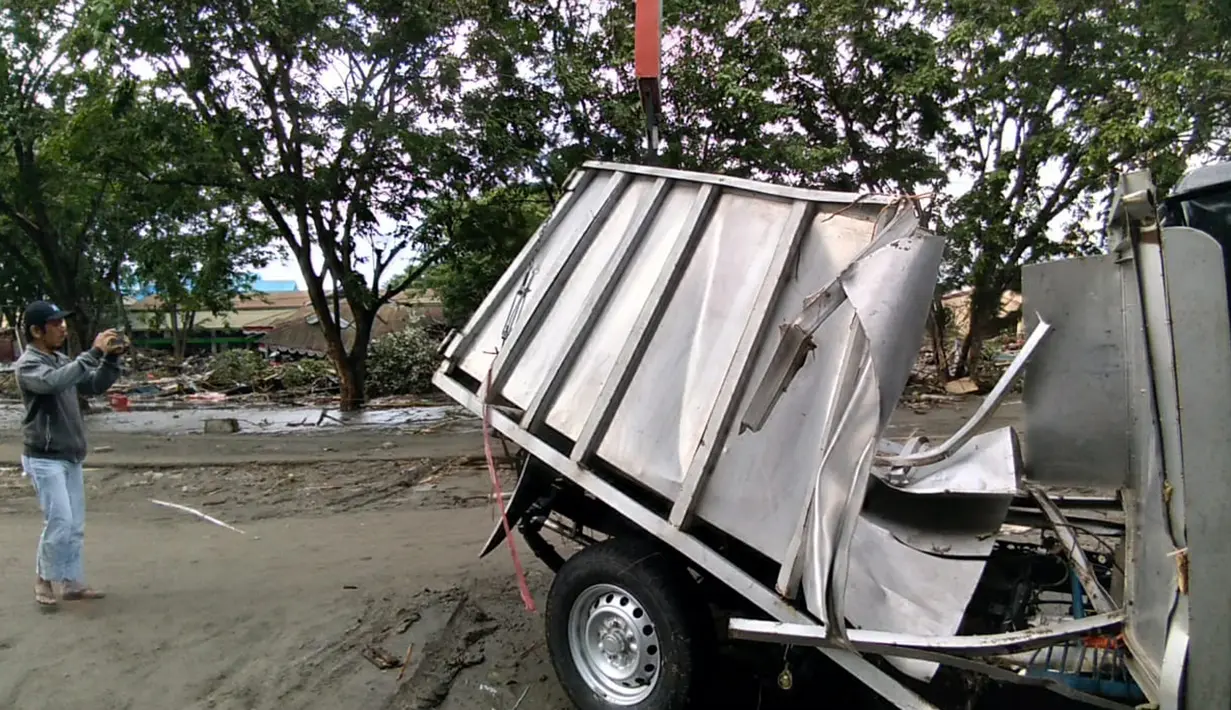 Seorang pria mengambil gambar kendaraan yang rusak akibat gempa dan tsunami di Palu, Sulawesi Tengah , Sabtu (29/9). Gelombang tsunami setinggi 1,5 meter yang menerjang Palu terjadi setelah gempa bumi mengguncang Palu dan Donggala. (AFP /OLA GONDRONK)