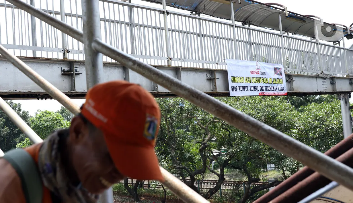 Pejalan kaki melintasi Jembatan Penyeberangan Orang (JPO) di Jalan Raya Lenteng Agung, Jakarta, Selasa (17/3/2020). Sebuah spanduk berisi ajakan menghindari kerumunan dan kumpul-kumpul untuk mencegah penyebaran virus Corona COVID-19 terpasang di JPO teresebut. (Liputan6.com/Helmi Fithriansyah)