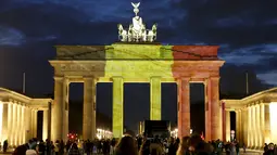 Sejumlah orang berdiri di depan gerbang Brandenburg di Berlin, Jerman, yang berubah warna menjadi bendera Belgia, Selasa (22/3). Hal itu sebagai bentuk penghormatan terhadap korban serangan bom Brussels. (REUTERS/Fabrizio Bensch)