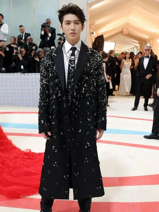 Cai Xu Kun tampil stunning dengan mantel sampai dasi dengan detail bling bling dari Prada. Lengkap dengan aksesori kipas bertulisan Tiongkok dalam genggaman penyanyi dan rapper asal China ini. [@themetgalaofficial]
