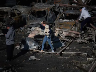 Seorang wanita menggendong anjingnya saat berjalan melewati mobil-mobil yang terbakar sehari setelah serangan udara Israel di Beirut, Lebanon, Kamis 9 April 2026. Israel terus melancarkan serangan besar-besaran terhadap Lebanon. (AP Photo/Emilio Morenatti)