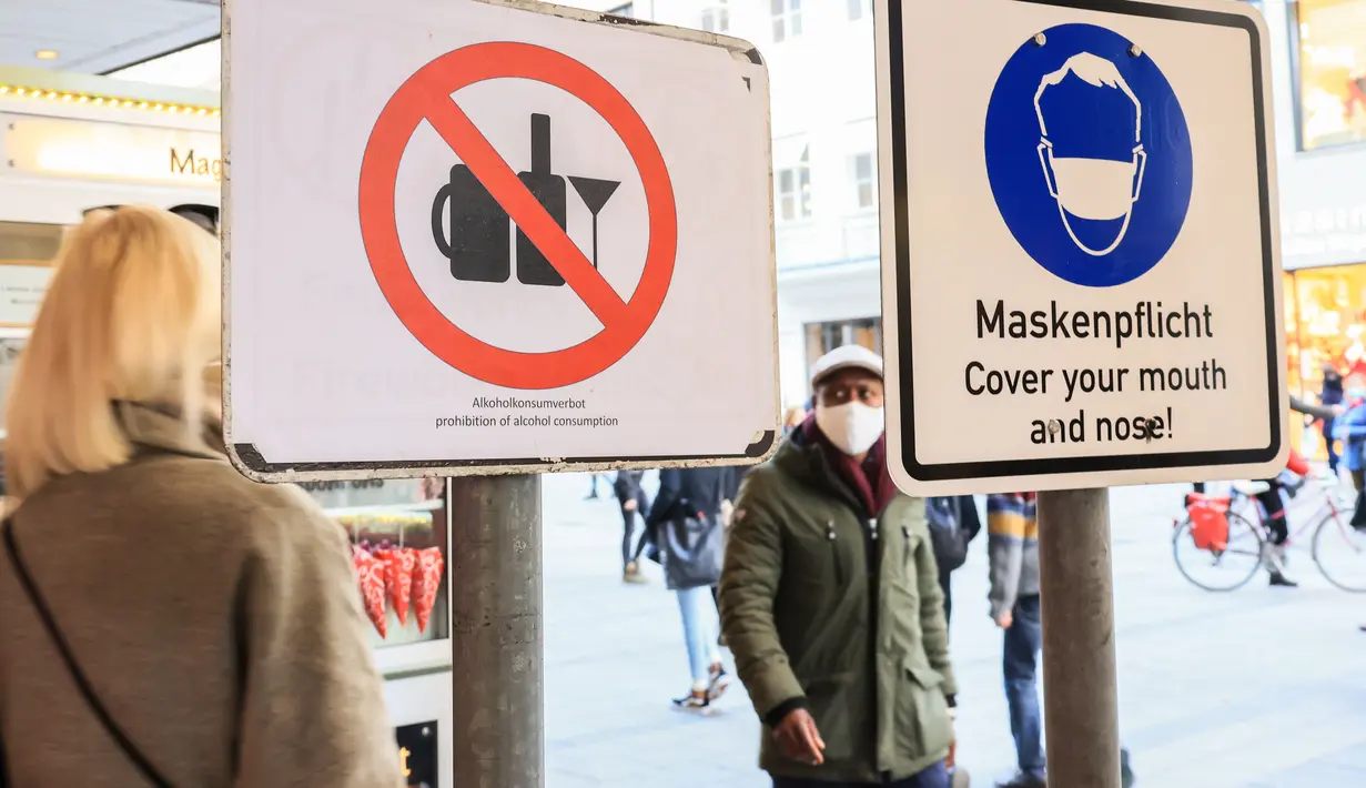 Para pejalan kaki berjalan melewati tanda yang mengingatkan warga untuk memakai masker dan larangan mengonsumsi alkohol di Munich, Jerman (11/12/2020). Kasus penularan dan kematian harian COVID-19 di Jerman terus meningkat dan mencapai rekor tertinggi baru. (Xinhua/Philippe Ruiz)