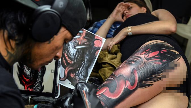 Seorang wanita terbaring saat membuat tato dikakinya selama Expotattoo Colombia 2019 di Medellin, departemen Antioquia (2/6/2019). Para penggila tato antusias untuk mentato tubuhnya di festival tato terbesar di negara tersebut. (AFP Photo/Joaquim Sarmiento)