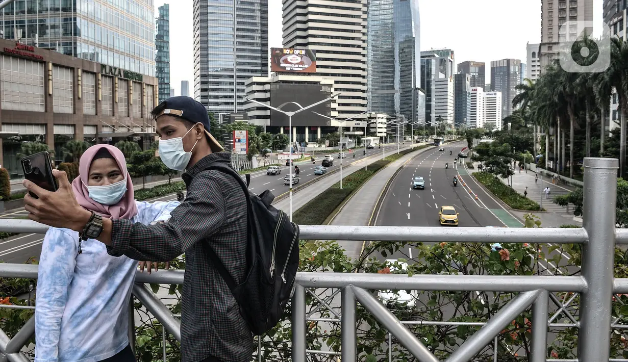 Sepasang warga berswafoto di JPO tanpa atap di kawasan Sudirman, Jakarta, Minggu (4/4/2021). JPO tanpa atap masih menjadi wisata alternatif warga ibu kota dalam menghabiskan waktu akhir pekan untuk berfoto-foto dengan latar belakang gedung perkantoran. (merdeka.com/Iqbal S Nugorho)