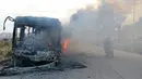 Pengendara motor melewati bus yang diserang dan dibakar saat dalam perjalanan ke al-Foua dan Kefraya di dekat Idlib, Suriah, Minggu (18/12). Bus itu sedianya untuk mengevakuasi warga yang sakit dan terluka di Aleppo timur. (REUTERS/Ammar Abdullah)
