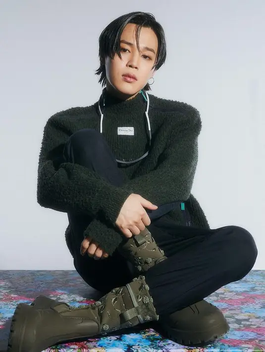 Berpose sambil duduk, Jimin BTS tampil gaya mengenakan busana bernuansa gelap. Ia memakai sweater rajut hijau tua dipadu dengan celana panjang biru dan bot yang sama di foto sebelumnya.  (Instagram/dior)