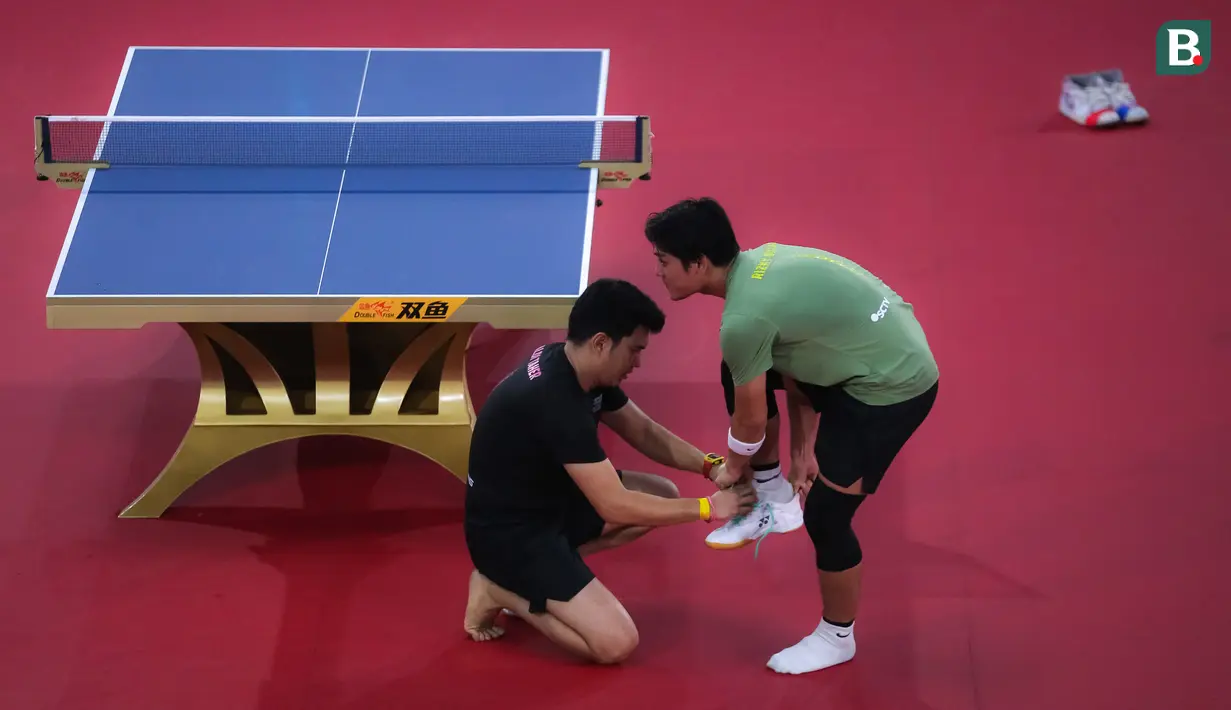 Selebritas Aldi Taher memakaikan sepatu ke Rizky Billar saat laga tenis meja Turnamen Olahraga Selebriti Indonesia (TOSI) di GOR UNJ, Jakarta, Minggu (16/07/2023). Aldi Taher kalah tiga set langsung dari Rizky Billar dengan skor 12-21, 15-21, 11-21. (Bola.com/Bagaskara Lazuardi)