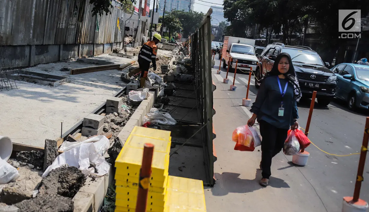 Warga melintas di samping proyek revitaslisasi trotoar di kawasan Cikini, Jakarta, Senin (1/7/2019). Revitalisasi trotoar di kawasan Cikini hingga Kramat ditargetkan rampung pada Desember 2019. (Liputan6.com/Faizal Fanani)