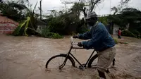 Seorang warga menuntun sepedanya saat melintasi banjir yang disebabkan oleh hantam Badai Matthew di Haiti (4/10). Keganasan Badai Matthew ini telah meluluhlantakkan wilayah Haiti. (REUTERS/Andres Martinez Casares)