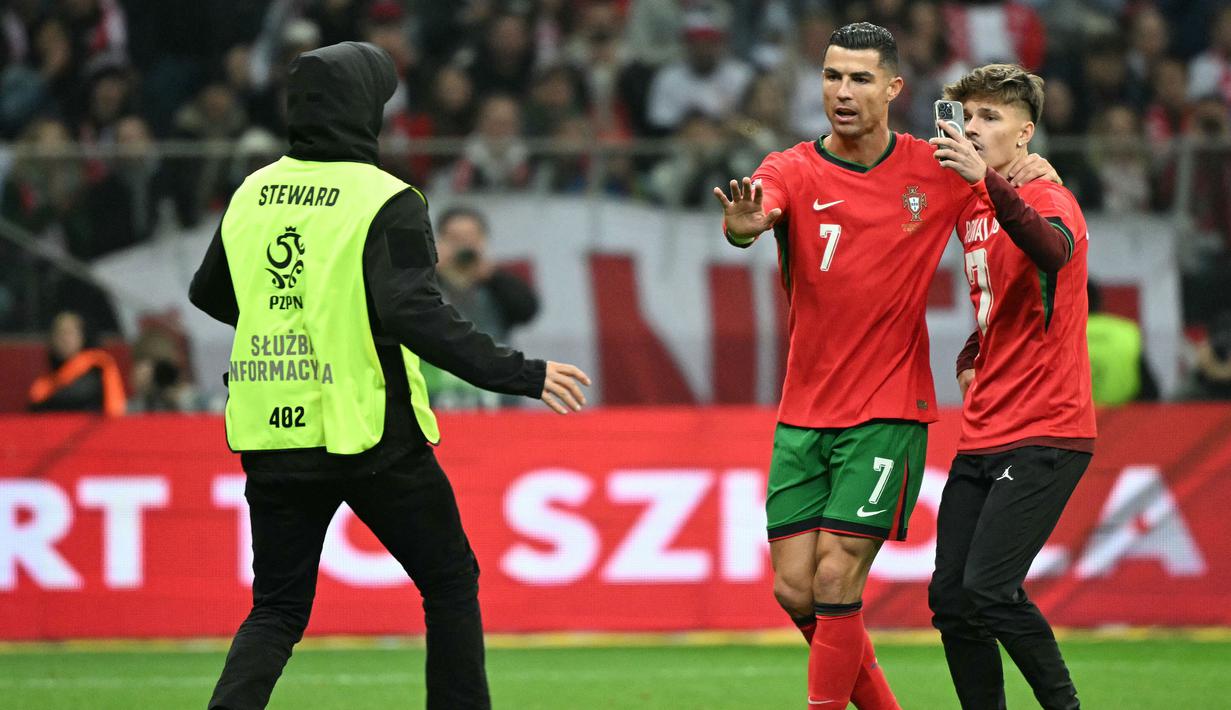 Pemain Portugal, Cristiano Ronaldo (tengah) menahan pihak keamanan yang akan menangkap seorang penyusup lapangan saat laga lanjutan EUFA Nations League Polandia di National Stadium, Warsawa, Polandia, Minggu (13/10/2024) WIB. (AFP/Sergei Gapon)