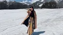 Bukan kimono, Yura justru tampil kece dengan kain lilit dipadukan long coat cokelat dan innernya saat berada di tengah hamparan salju.  Credit: Instagram (@yurayunita)