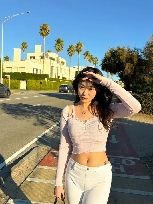 Saat berada di Melbourne, Australia, Livy memilih crop top lengan panjang berwarna pink muda dengan detail renda, dipadukan dengan celana putih. Paduan warna yang cerah ini menciptakan kesan segar dan stylish, memancarkan pesonanya sebagai fashionista muda. Dengan latar deretan pohon palem di jalan raya, Livy tampak effortless namun tetap mencuri perhatian. (Liputan6.com/IG/@livyrenata)