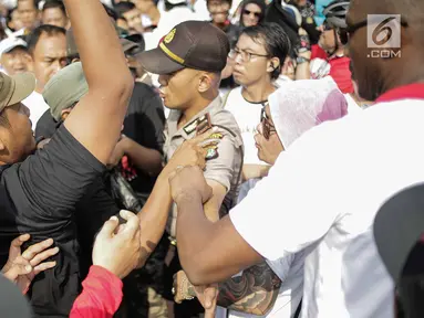 Seorang aparat kepolisian berusaha memisahkan massa berkaus #2019GantiPresiden dan #DiaSibukKerja yang saling sindir saat bertemu pada kegiatan Car Free Day di sisi barat Bundaran HI, Jakarta, Minggu (29/4). (Liputan6.com/Faizal Fanani)