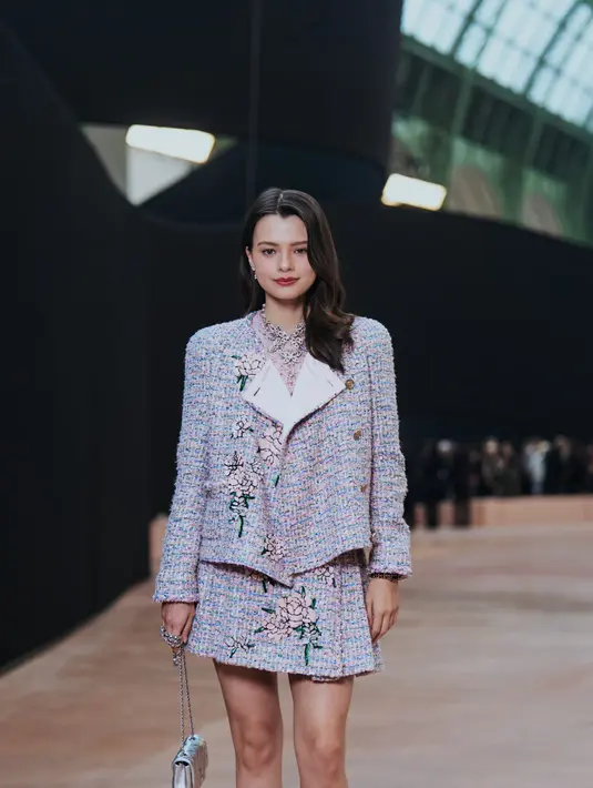 Rebecca Amstrong tampil borjuis dengan setelan open lid jacket dan rok mini tweed bermotif bunga. Ia terlihat jinjing Flap Bag mini silver sebagai aksesori [Chanel]
