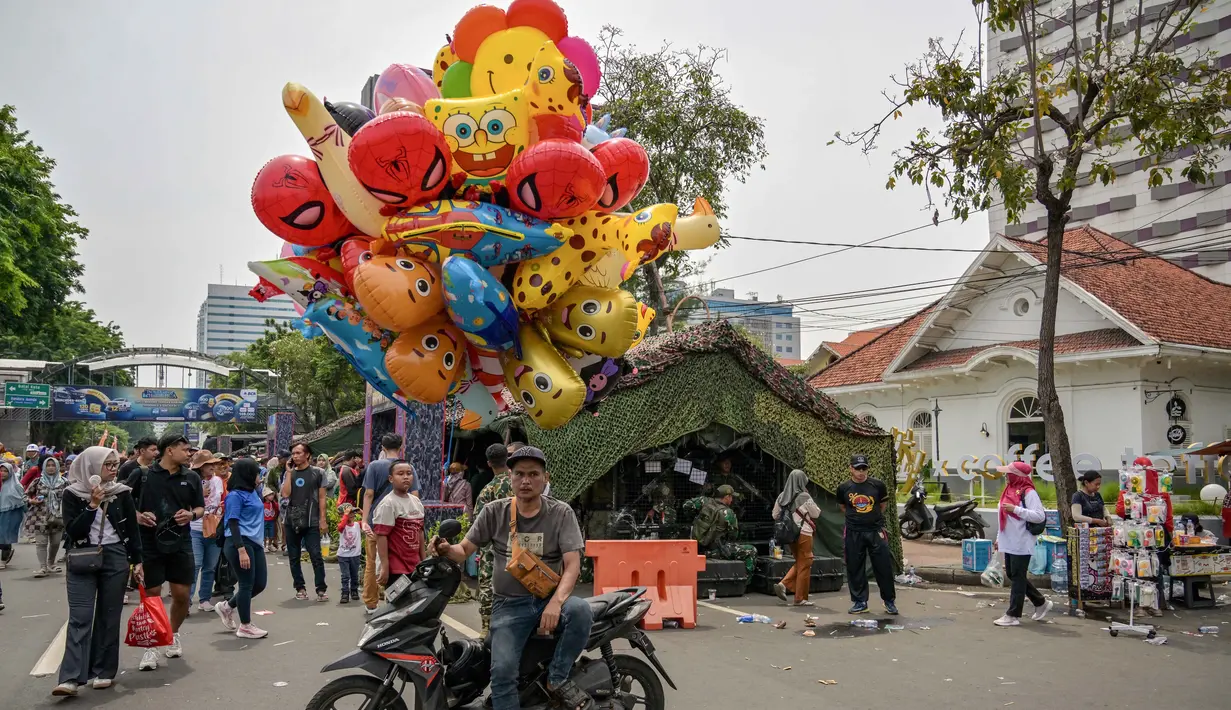 Masyarakat dapat melihat langsung dari dekat dan berfoto dengan alutsista tersebut. Tampak dalam foto, seorang penjual balon menunggu pelanggan sementara pengunjung berfoto dengan kendaraan militer selama Pameran Marinir Indonesia, yang menandai peringatan Hari Ulang Tahun ke-80 Korps Marinir TNI AL di Surabaya, Jawa Timur pada Minggu 9 November 2025. (JUNI KRISWANTO/AFP)