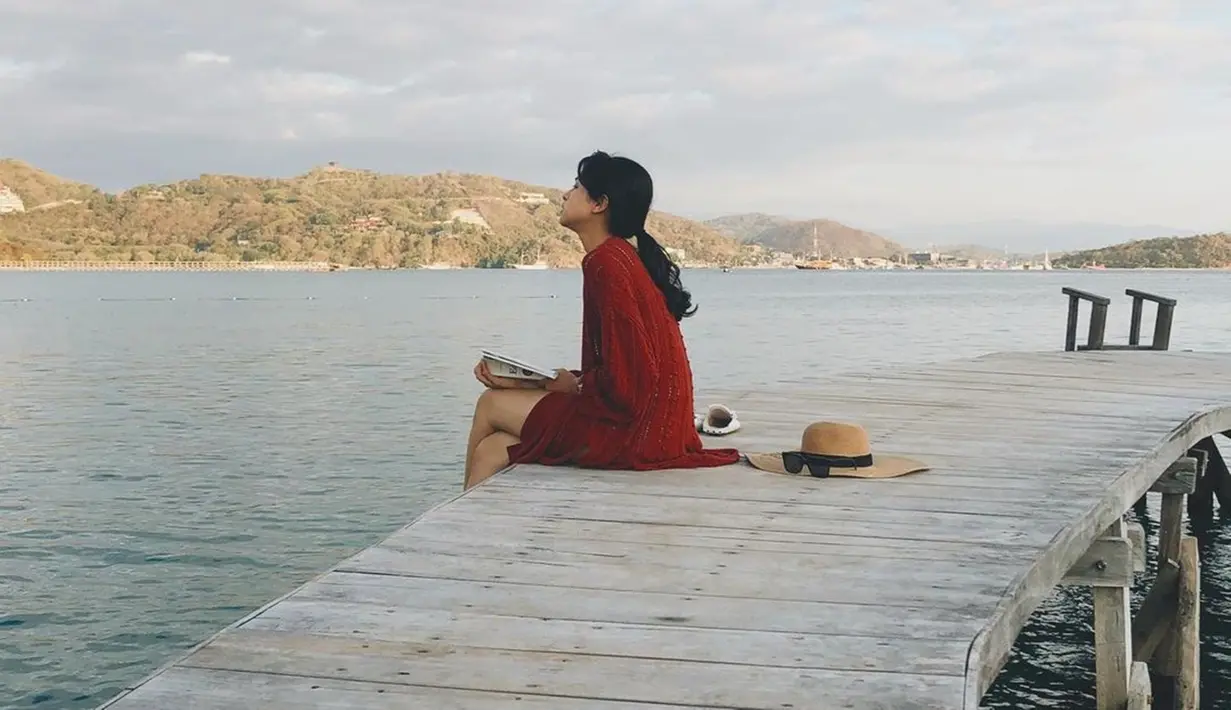 Membaca buku sambil menikmati alam bisa menjadi cara menarik untuk Maudy Ayunda melepas penat. Buku yang dibaca benar-benar disempurnakan oleh tempat yang indah di alam bebas. Hamparan laut yang tenang menambah kesan hening sehingga cocok jadi spot membaca buku. (Liputan6.com/IG/@maudyayunda)