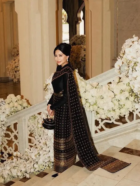 Dengan atasan hitam lengan panjang, dipadukan kain bermotif keemasan untuk rok panjang dan selendangnya. Ia pun membawa tas model bundar hitam yang unik.  [@janetira]