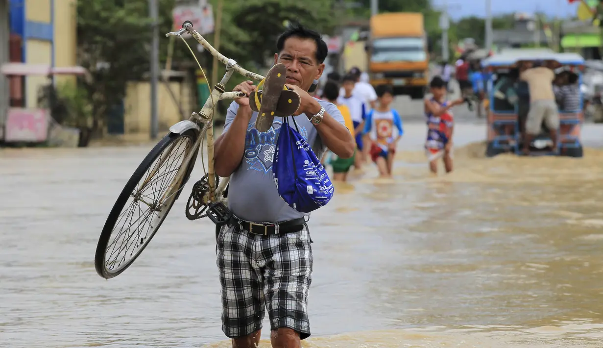 Seorang pria membawa sepeda menyebrangi banjir setelah hujan lebat di Kota Candaba, Pampanga, Manila, Filipina (17/12). Sembilan orang tewas akibat bencana yang terjadi di Filipina. (REUTERS/Romeo Ranoco)