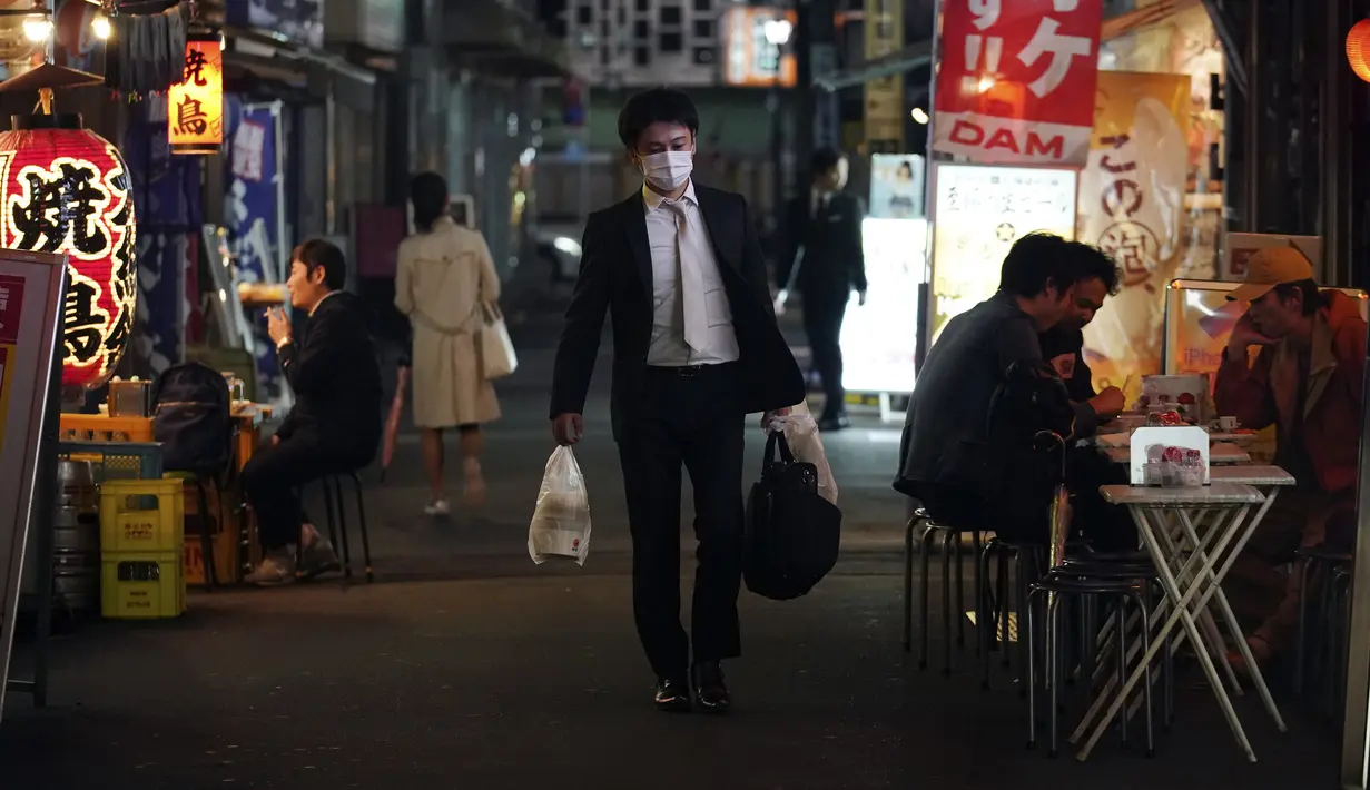 Seorang pria yang mengenakan masker berjalan mlewati bar jalanan di Tokyo, Jepang, 28 April 2020. Pandemi virus corona COVID-19 mengadu kelompok yang bersedia mengikuti peraturan tetap tinggal di rumah dengan mereka yang menolaknya. (AP Photo/Eugene Hoshiko, File)