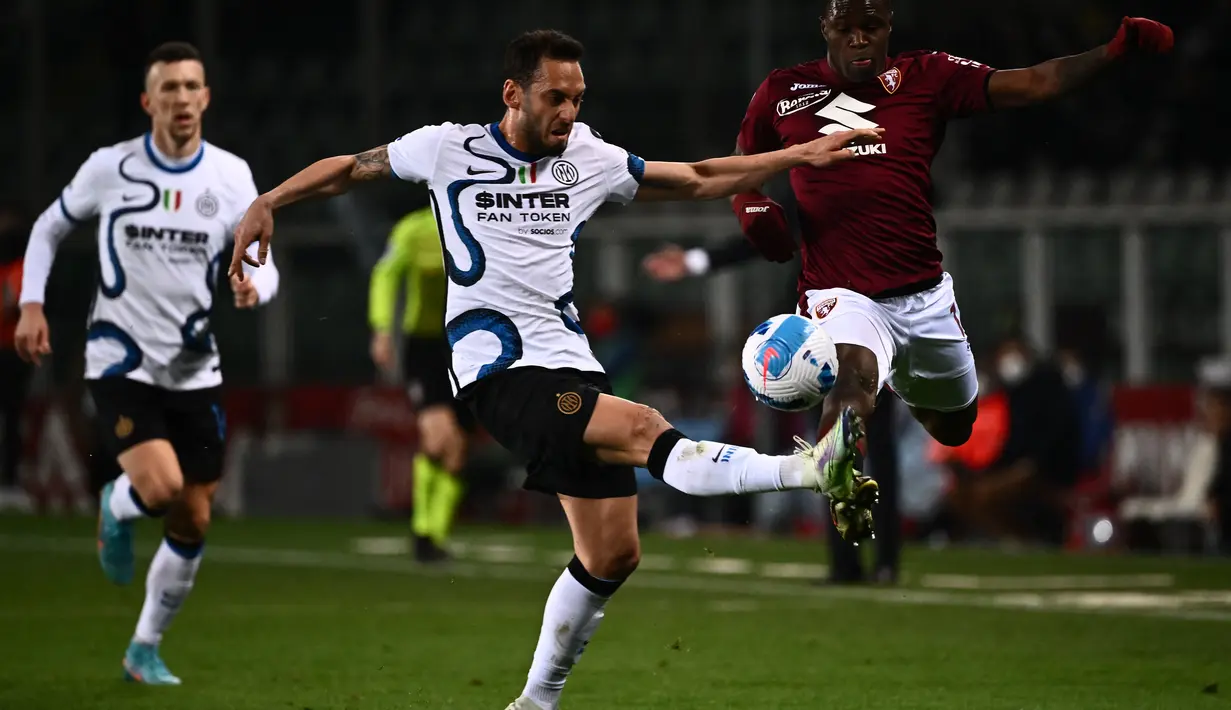 Gelandang Inter Milan, Hakan Calhanoglu (tengah) dan bek Torino Pantai Gading Wilfried Singo (kanan) berebut bola selama pertandingan lanjutan Liga Serie A Italia di stadion Olimpiade di Turin, Senin (14/3/2022). Dengan hasil ini Inter Milan turun ke peringkat ketiga dengan 59 poin. (AFP/Marco Berto
