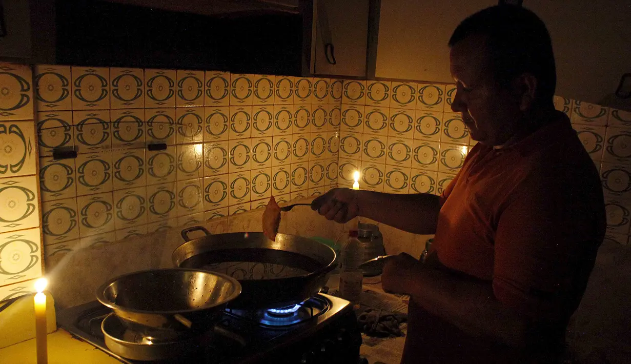 Seorang pria memasak di dekat lilin akibat pemadaman listrik di San Cristobal, Venezuela, Senin (25/4). Pemadaman berlangsung selama 40 hari karena negara tengah berjuang dari kekeringan parah yang membatasi hasil PLTA. (REUTERS/Carlos Eduardo Ramirez)