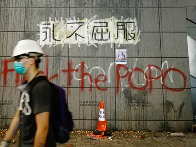 Seorang demonstran berjalan melewati markas polisi yang ditulisi 'Never Give In', Hong Kong, Jumat (21/6/2019). Markas polisi tersebut jadi korban aksi vandalime demonstran dalam lanjutan aksi unjuk rasa menolak RUU Ekstradisi. (AP Photo/Vincent Yu)