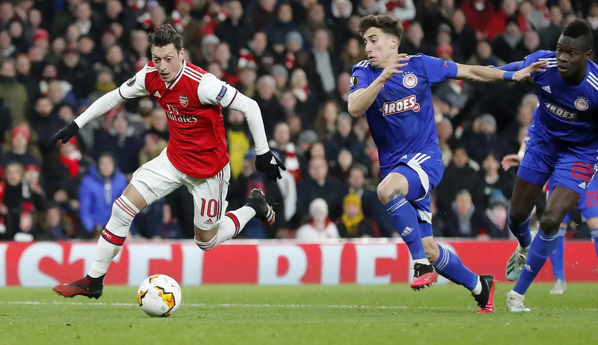 Gelandang Arsenal, Mesut Ozil menggiring bola dari kejaran pemain Olympiakos, Kostas Tsimikas  pada pertandingan leg kedua babak 32 besar Liga Europa di stadion Emirates, London, Kamis (27/2/2020).  Olympiakos menang 2-1 dan lolos dengan unggul agregat gol tandang 2-2. (AP Photo/Frank Augstein)