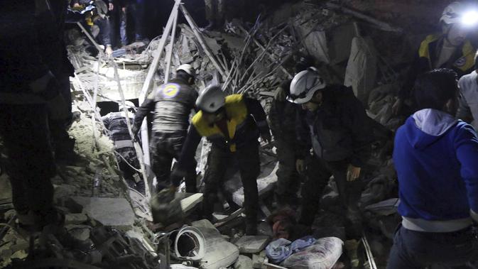Relawan White Helmets menyingkirkan reruntuhan bangunan untuk mencari korban serangan militer di Provinsi Idlib, Suriah, Minggu, (7/1). Selain menewaskan 25 orang, serangan ini juga melukai 100 lainnya. (Syrian Civil Defense White Helmets via AP)