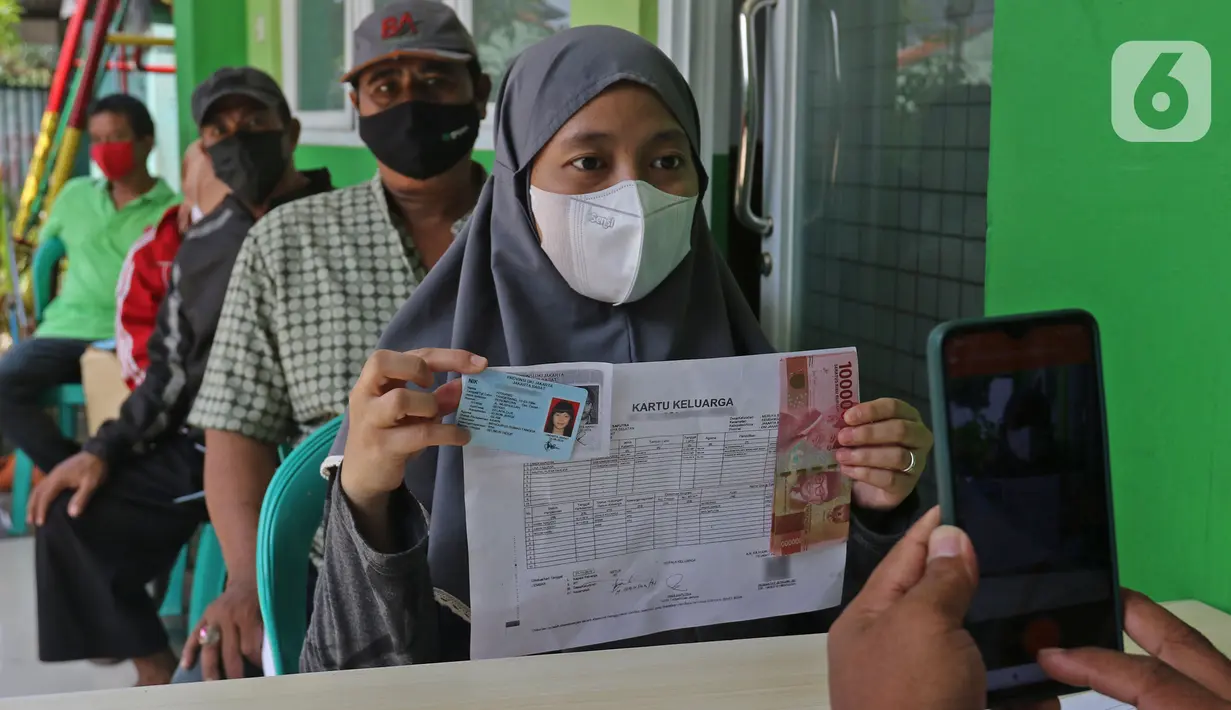 Petugas memotret warga penerima Bantuan Sosial Tunai (BST) di kawasan Kelurahan Kembangan, Meruya, Jakarta Barat, Minggu (25/07/2021). Kementerian Sosial melalui PT Pos Indonesia mulai menyalurkan BST yang dirapel dua bulan sekaligus dengan total Rp600ribu. (Liputan6.com/Herman Zakharia)