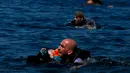Seorang pengungsi Suriah menggendong bayi sambil berenang menuju pantai setelah perahu yang mereka naiki kempes sebelum mencapai pulau Yunani Lesbos, 12 September 2015. (REUTERS/Alkis Konstantinidis)  