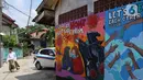 Warga berjalan di depan mural bertema virus corona COVID-19 yang menghiasi dinding rumah di kawasan Pangkalan Jati Baru, Depok, Jawa Barat, Selasa (2/6/2020). Mural bertulis ‘Stay At Home, Keep Safe From COVID-19’ itu untuk mengingatkan warga akan bahaya COVID-19. (Liputan6.com/Johan Tallo)
