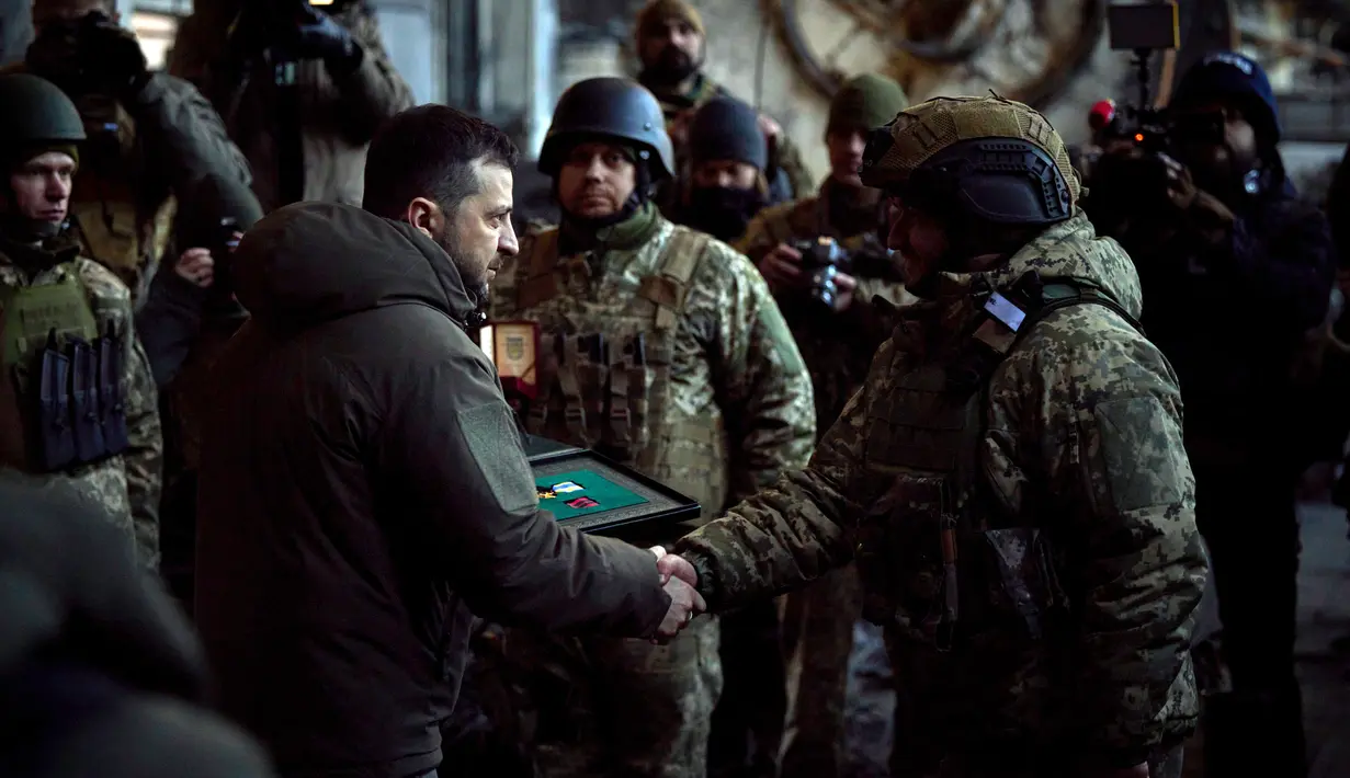 Presiden Ukraina Volodymyr Zelenskyy (kiri) memberikan penghargaan kepada seorang tentara di lokasi pertempuran terberat dengan melawan Rusia di Bakhmut, Ukraina, 20 Desember 2022. Bakhmut tetap berada di tangan Ukraina selama serangan Rusia. (Ukrainian Presidential Press Office via AP)