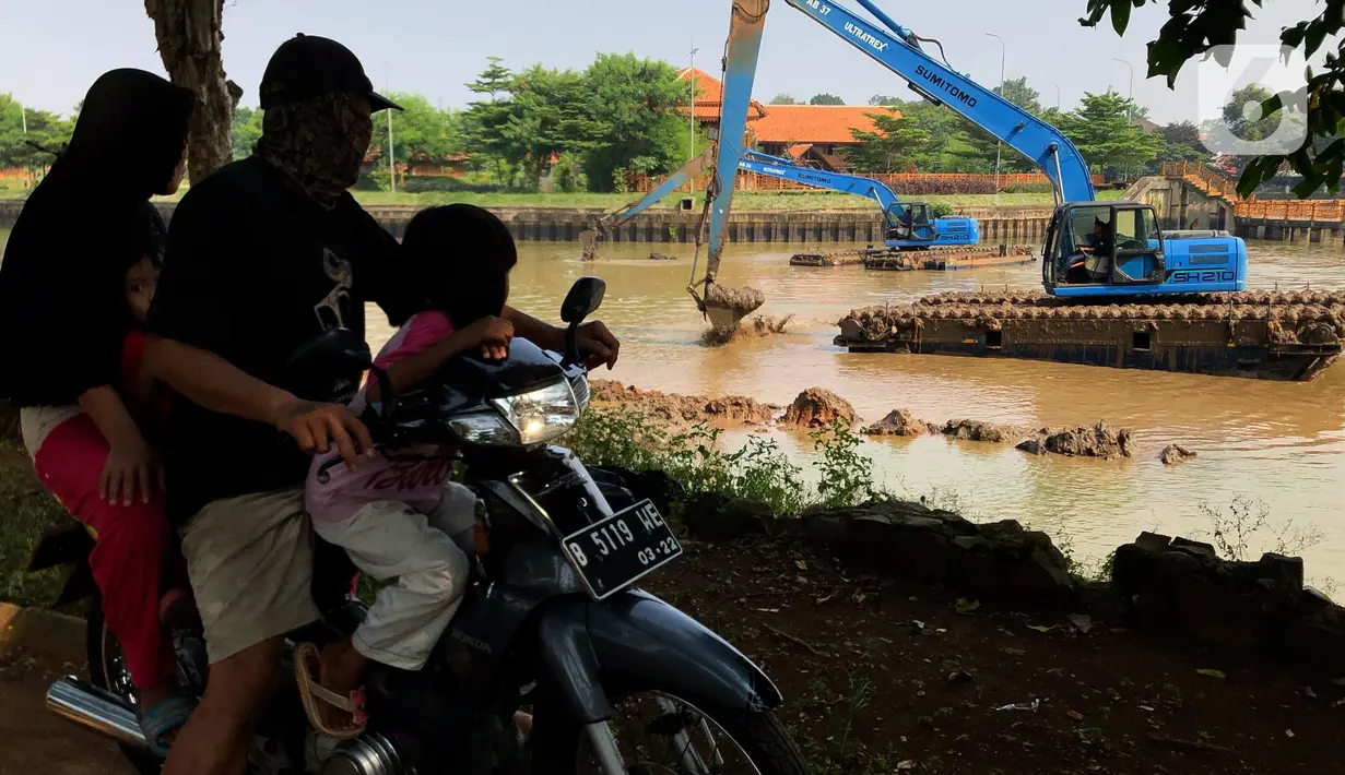 Pengendara motor melintas saat alat berat mengeruk lumpur di Setu Babakan, Jakarta, Selasa (30/6/2020). Pengerukan dilakukan guna mengembalikan kedalaman setu sehingga menambah daya tampungnya. (Liputan6.com/Immanuel Antonius)