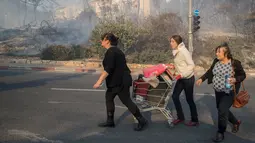 Sejumlah warga menyelamatkan diri dari kebakaran hutan hebat yang melanda kota utara Israel, Haifa, Kamis (24/11). Kebakaran parah telah menyebabkan kerusakan yang belum pernah terjadi sebelumnya di kota terbesar ketiga Israel itu. (JACK GUEZ/AFP)