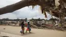 Kondisi kesehatan warga juga semakin terancam. Tampak dalam foto, para penyintas berjalan melewati puing-puing di area yang hancur akibat banjir bandang di Aceh Tamiang, Pulau Sumatra, Jumat 5 Desember 2025. (AP Photo/Binsar Bakkara)