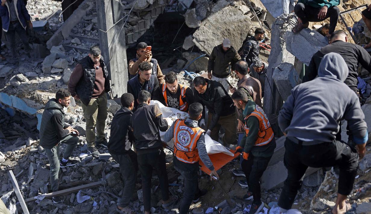 Untuk diketahui, hingga awal Februari 2026, berdasarkan data kementerian kesehatan di Gaza, jumlah total korban tewas mencapai 71.769 orang yang mayoritas wanita dan anak-anak. Sementara, ada lebih dari 171.483 orang mengalami luka-luka. Tampak dalam foto, para penyelamat membawa jenazah seorang korban di tengah reruntuhan kantor polisi Sheikh Radwan di Kota Gaza pada 31 Januari 2026. (Omar AL-QATTAA/AFP)