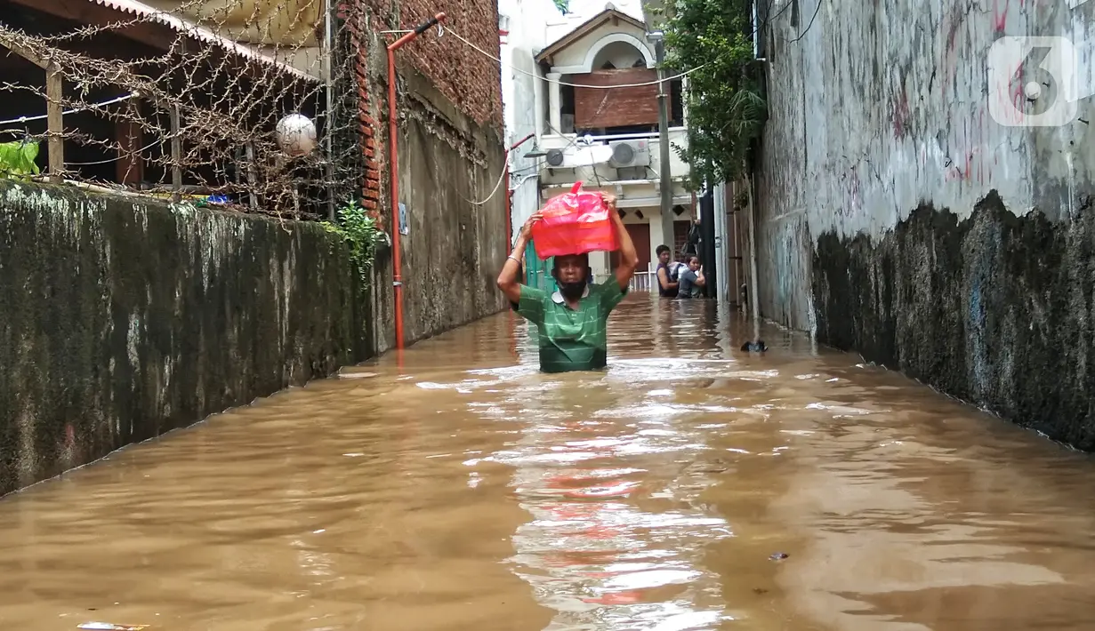 Warga berjalan menyusuri banjir yang merendam permukiman di kawasan Kebalen, Jakarta, Sabtu (20/2/2021). Curah hujan yang tinggi menyebabkan banjir setinggi orang dewasa di kawasan Kebalen. (Liputan6.com/Johan Tallo)