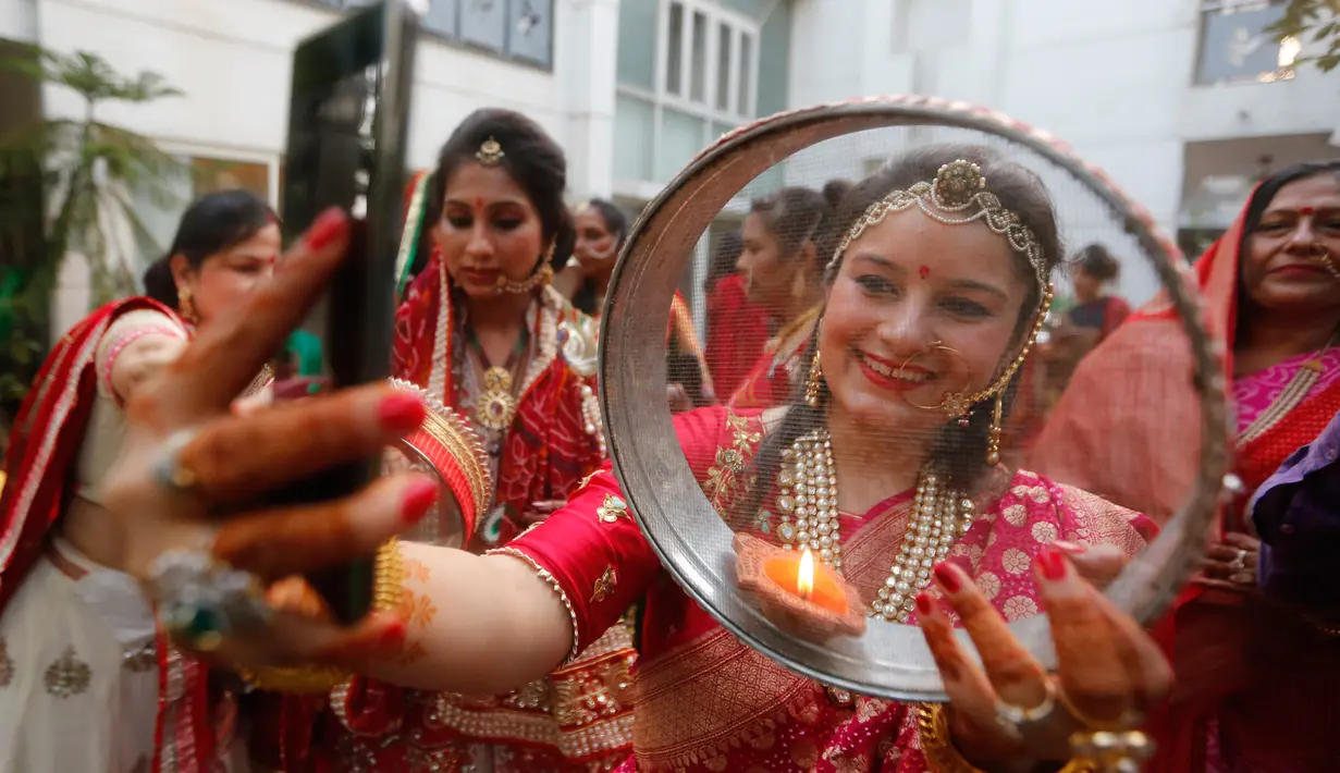 Seorang wanita Hindu memandangi foto suaminya di ponsel ketika melakukan ritual festival Karva Chauth di Ahmadabad,  Kamis (17/10/2019). Selama festival, wanita-wanita yang sudah menikah di India berpuasa sepanjang hari dan memohon umur panjang serta keselamatan untuk suami mereka. (AP/Ajit Solanki)