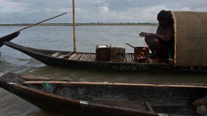 Nelayan menghangatkan tangannya di atas kapal di tepi sungai Brahmaputra di Jorhat, India (3/4). Brahmaputra adalah salah satu sungai terbesar di Asia, yang melewati wilayah China Tibet, India dan Bangladesh sebelum konvergen ke Teluk Benggala. (AP Photo/Anupam Nath)