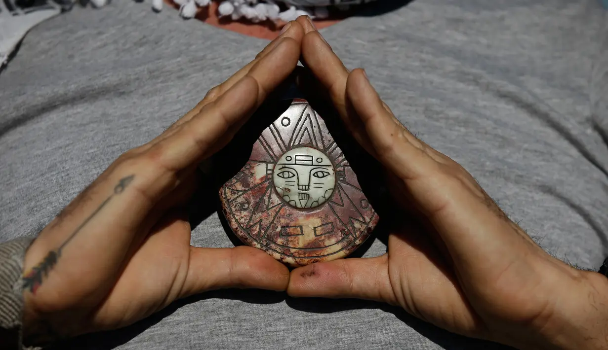 Seorang pria Meksiko memegang jimat dari Peru ke dadanya saat mengikuti perayaan equinox musim semi di situs arkeologi Teotihuacan, Meksiko (21/3). Ritual ini dipercaya bisa mengalirkan energi positif serta mengusir roh jahat. (AP Photo/Rebecca Blackwell)